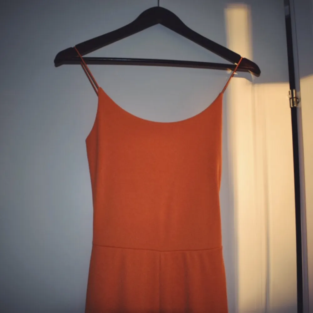 En splitterny orange jumpsuit som kan användas till vardags och även på festliga tillfällen. . Övrigt.