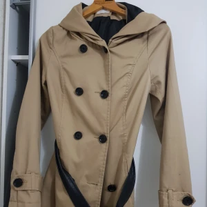  - Beige kappa med svarta knappar och svart läder bälte.  Kappan har även luva.  