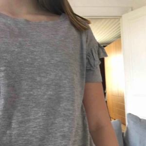  - Fin grå T-shirt med volang på ärmen.
