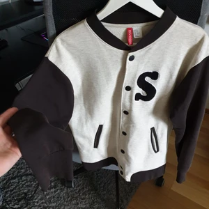 College jacka  - En tröja i college jacket modell med Santiago tryck bak och S fram. Storlek S men är större känns som M, L. Begagnad och håll i ena fickan. Frakt tillkommer