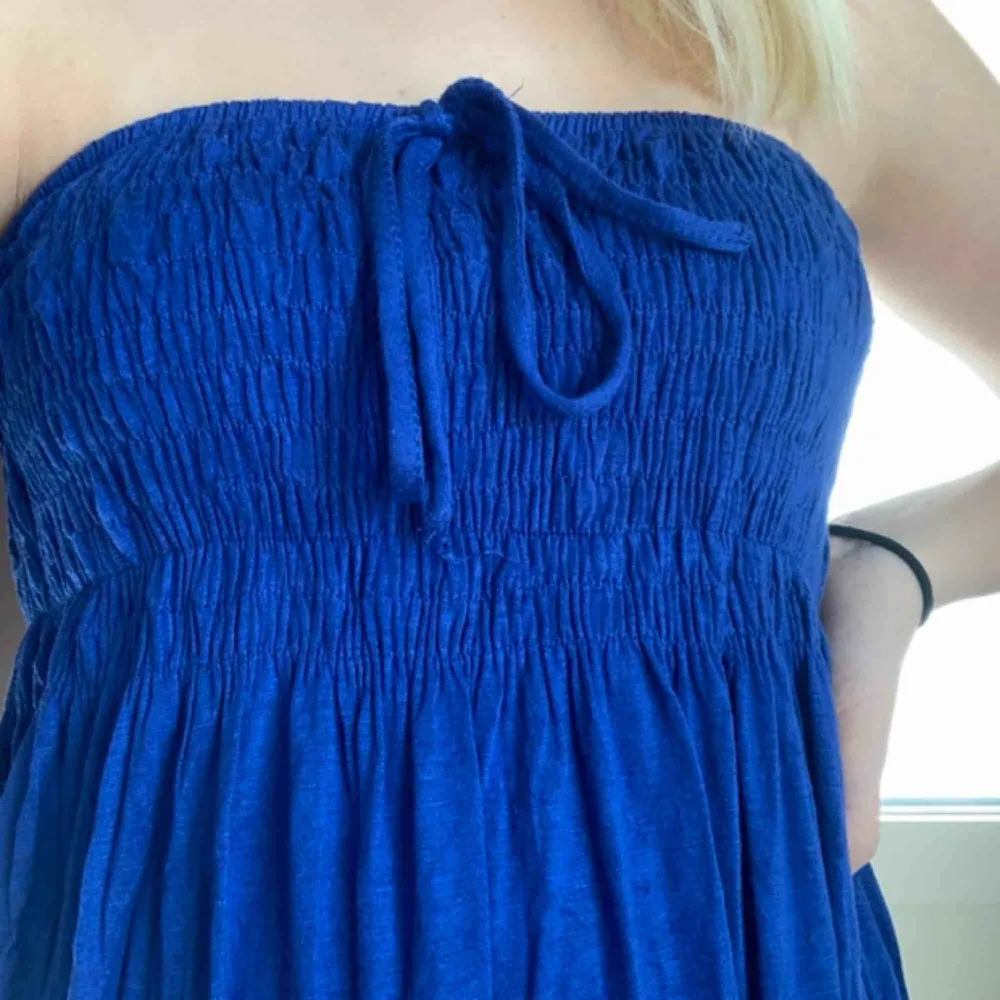 Söt blå klänning utan axelband. Man kan välja att knyta snöret runt halsen, som rosett eller gömma det innanför klänningen. Köparen står för frakten. Köpt i USA. Klänningar.