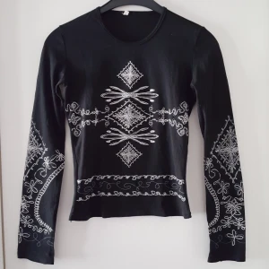 Vintage mönstrad svart tröja - Vintage svart tröja med vitt mönster. Storlek M, men är rätt liten i storleken och uppskattar den mer till en väldigt stretchig XS/S. Är lite tunnare tyg, typ som mesh fast inte genomskinlig. Fraktkostnad blir 47kr.
