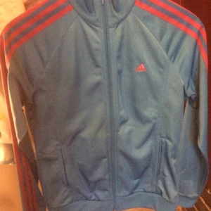  - Oanvänd Adidas-tröja i oanvänt skick. I fina färgerna blått med rosa ränder.