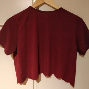  - Fin croptop o vinrött stretchigt material. Passar perfekt till vår och sommar! Scallop-hem men delarna omlott i bak så blir halvöppen rygg. Används ej pga för liten. Behövde sy kragen när ja använde den förr men är ej bra på att sy>>prissänkning. Syns dock ej så mycket 