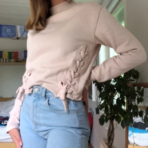 Rosa tröja med snörnings detaljer - En ljust rosa tröja med jätte gulliga snörnings-detaljer. Storlek 34