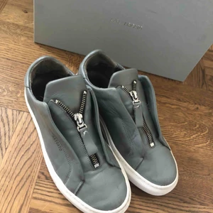  - Ett par axel arigato skor i modell Clean 90 Zip sneaker. Använda en vår ungefär. Världens bekvämaste sko. Dragkedjan sitter fast och går inte att öppna men de sitter jättebra ändå och är super smidiga att sätta på.   Inköpspris: 1800kr