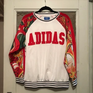 Adidas Sweater Rito Ora kollektion - Adidas tröja i lite glansigare material, Rita Oras kollektion. Använd sparsamt! Storlek 36 men är oversize i modellen så passar även 38/40 beroende på hur man vill att den sitter. Eventuell frakt tillkommer isf (59kr) betalas av köparen!