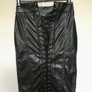 Kjol i svart fejkskinn  - Supecool stretchig knä-lång kjol i fejk-skinn som sitter som en smäck! Har aldrig använt för har inte hittat ett tillfälle för det. Riktigt bra passform och följer kroppen väldigt snyggt. Passar XXS-M beroende på hur ”öppen” den ska vara i snörningen. 