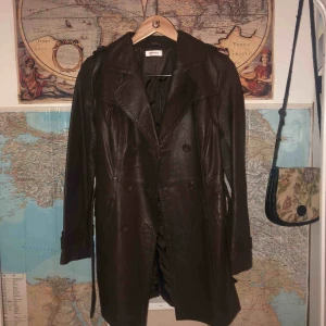  - Brun läderkappa med skärp som går ner till låret. Nästan helt oanvänd, extraknappar finns på insidan. 200kr eller högst bjudande
