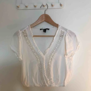  - Vit blus med virkade detaljer - aldrig använd. Den är i storlek M och i nyskick, förutom en liten, liten strimma från en bläckpenna som råkat komma åt (se bild 2).