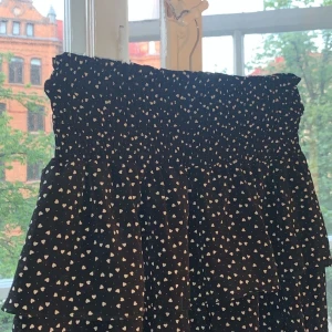 Kjol med vita hjärtan  - Volang kjol med vita hjärtan och resårband. Storlek L men liten i storlek skulle säga att den passar S/L FINNS INTE KVAR