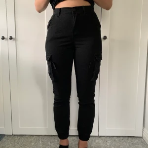 Svarta cargobyxor - Snygga cargobyxor i stretchmaterial med fickor på sidan. Använda endast en gång, så dom är i princip nya✨ Jag är 175cm lång, så lite korta men annars sitter dom perfekt. Det är en storlek XS men sitter mer som en 36/38. Frakt på 49kr tillkommer 💕