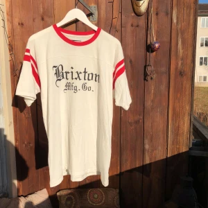  - Vit t-shirt med röda ränder. Köpt i Brixton, England. Hel och ren.  Stor-rensar hemma, alla mina plagg kostar 50kr / 3st för 100kr. Möts upp i Sthlm/Uppsala, annars tillkommer frakt. 
