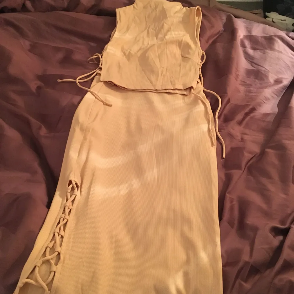 Matchande set i ljusrosa/dusty pink. Oanvänd. Modellen är tight, och har snörning på sidorna. Toppen är crop top och kjolen har hög midja. Toppen är storlek 34, och kjolen storlek 36 . Mekot.