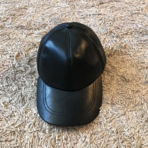  - Keps från Nelly i skinnimitation. Justerbar band på baksidan. Köparen står för eventuell frakt. 