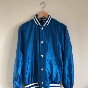  - Tunn blå jacka i storlek S i dam modell.  Vit-randiga muddar och vita knappar.  Något oversize.  Gjord i 100% polyester. 