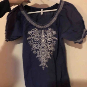  - Gullig blå blus med vita broderier och täckta knappar! Stor i storleken så passar även M!