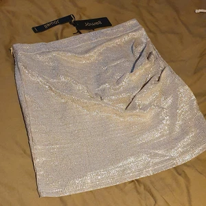 Skimrande kjol - Helt ny, oanvänd minikjol från Jöwell Paris. Denna är superfint skimmramde i guld och silver med en ruched detalj som ger kjolen "vågor". Den har dragkedja på sidan som knappt syns.  
