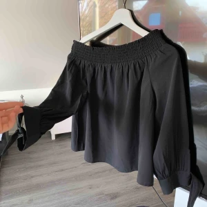  - Svart ofshoulder blus från ginatricot med fina rosetter på armarna 