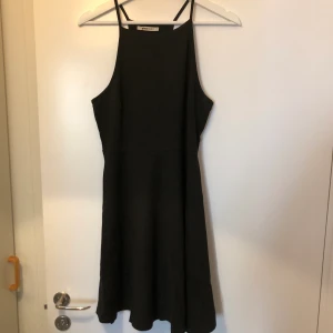 Svart kortklänning - Svart knälång klänning med halterneck. Tajt över bröst och går ut vid midjan. Fint skick!