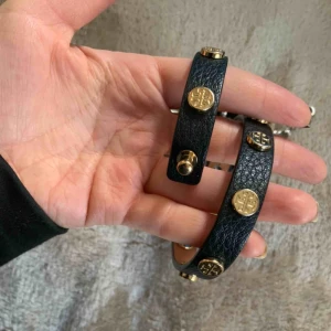  - Tory burch armband i absolut nyskick. Svart läder med guld detaljer. Den går 2 varv.  Frakt (43kr)🌸 Nypris 800kr.