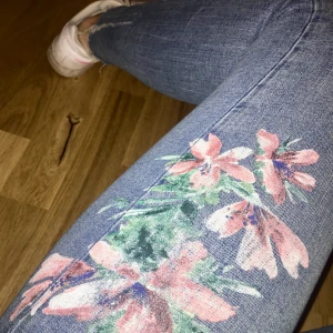 Jeans med tryck  - Coolaste jeansen med blomtryck på vänstra låret. Fint skick förutom att lappen är lite lös 💕💕 jag är ca 160 och har 36 i vanliga fall 