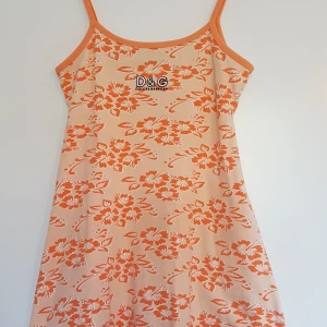 Dolce&Gabanna klänning stl s/m - Orange Docle & Gabanna med blom motiv. Sparsamt använd. Mycket fint skick. Står ingen stl men skulle säga att den är s/m.