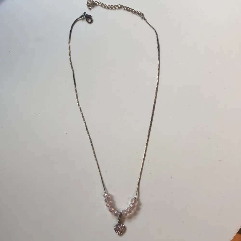 Halsband med hjärta och rosa pärlor. Kedjan är både ljus och mörk metall på.. Accessoarer.