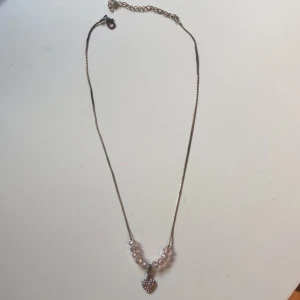 Halsband - Halsband med hjärta och rosa pärlor. Kedjan är både ljus och mörk metall på.