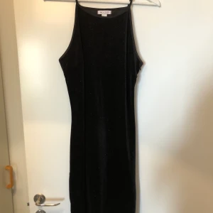 Svart festklänning - Svart kortklänning i diskret glitter. Dragkedja i ena sidan. Ihopdragen i bak för att ge snygg och putig rumpa. Har sytt igen ett litet hål i en söm i sidan, syns inte när klänningen är på. Kan visa bild vid önskemål Använd 1 gång!