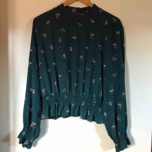  - Jättefin petrolgrön och blommig blus från förra årets kollektion på H&M. Knäppning i nacken och volang vid ärmslut och nederkant. 100% polyester. Strl 44 men ganska liten i storlek. Använd en gång. 