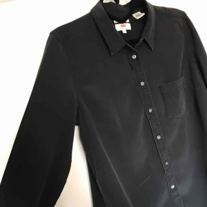  - Skjorta i 100% silke. Den ser inte direkt ut som på bilden, det var väldigt svårt att göra den rättvis. Skjortan är lite glasig i tyget och den har jämn svart färg. På bilden ser den ojämn ut men så är det inte. Köpte den för ca 500kr