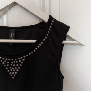  - Svart peplumtopp från MQ med stenar kring halsen. Fint skick! Stretchigt tyg, sitter bra även på mig som normalt är en S.  50% viskos, 48% polyester, 2% elastan.