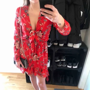  - Röd blommig klänning i chiffongtyg. Resår i midjan, reglerbar knytning framtill och volangkant nedtill. Helt oanvänd, i jättefint skick. Köparen står för frakten. Kan även mötas upp i Lidköping, Växjö eller Göteborg 🌹