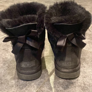 Svarta Uggs - Säljer dessa svarta Uggs med rosett där bak i storlek 38! Knappt använda så är i bra skick🤍🤍 köptes för ca 2000 men säljer för 1100