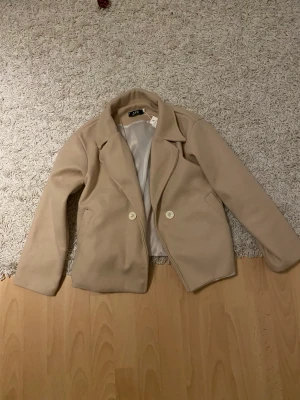 Kort vårkappa - Måste tyvärr sälja denna kappan eftersom den är för liten! Färgen är beige/ljusrosa, svinsnygg! Aldrig använd, lapparna kvar☺️Hör av er vid fler frågor eller bilder!  