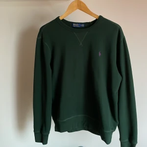 POLO RALPH LAUREN SWEATSHIRT  - Strlk M. Mörkgrön tröja i kvalitativt material med lila logotyp. Över 1000kr retail