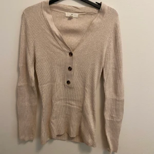 Beige långärmad tröja - En beige v ringad långärmad tröja med bruna knappar som funkar perfekt på sommarkvällar eller hösten.