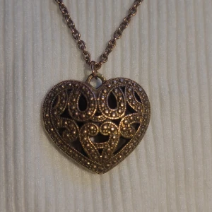 Vintage Hänge Hjärta Kopparlegering - Hej! Jag tänkte sälja mitt vintage hänge gjord av en koppar legering. Hjärtat har en vacker glans med fina detaljer och känns härligt att ha i handen. Måttet är 4x4cm och väger 35 gr. Kedjans längd är76-80cm och gjord av en slags metall. 70-80 talet.