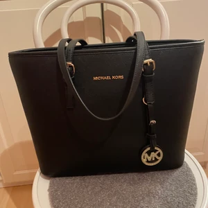Michael Kors Jet Set - Säljer nu min älskade MK Jet Set. Den är sparsamt använd men har en liten slitning på kanterna.   Finns en ficka inuti, perfekt att ha nycklar etc.   Rymlig och snygg till varje outfit för den svarta färgen.  Pris kan diskuteras vid snabb affär!