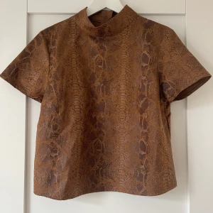 Blus med ormmöster i skinnliknande material - Säljer en blus i mörkbrunt ormmönster från Zara i storlek M, nästan helt oanvänd. Pris: 250.