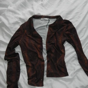 Blommig topp - Super fin brun topp från NAKD x Freja Wewer med blomm liknande mönster på! Den är helt oanvänd med alla lappar kvar på. Skriv för frågor eller fler bilder🍂