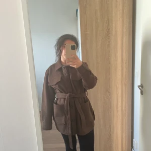 Brun kappa  - Säljer denna otroligt fina kappan. Den har fickor både uppe vid brösten och vid sidorna, storlek 36!  Perfekt i längden och kappan är endast använd en gång och är i ny skick från MQ. Pris 500 kr + frakt! Skriv till mig för intresse!