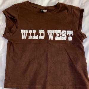 En brun T-shirt som är lite kortare och tajtare med trycket ”WILD WEST” köptes innan sommar starten och har använts Max 4 gånger. Köpte på HM. För frågor skriv grill mig privat Köparen står för frakten💗