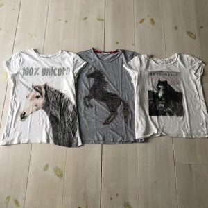 3 söta T-shirts med hästmotiv  - Säljer dessa 3 T-shirts tillsammans. Tröjan i mitten har ”vändbara” paljetter så att hästen kan skifta mellan rött och silver. väl använda men hela och rena. Storleken är från vänster till höger, alla 3 ungefär lika stora. Köparen står för frakten!
