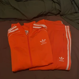 Adidasset - Oranget adidaset i bra skick! Använt fåtal gånger.  Kofta storlek: 164 men passar xs/s Byxor storlek: 36  Pris: 500kr  