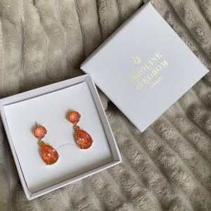 Caroline Svedbom - Slutsålda Caroline Svedbom mini drop örhängen i orange färg med lila/blått skimmer i färgen ”glow delite”. Silver och förgyllt med 18k guld. Aldrig använd. Jättefin present att ge bort! Ord. pris 795kr