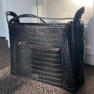 Svart väska - Svart rymlig väska i ormskinnsimitation från NAKD. Får plats med både dator (13”) och anteckningsblock om man vill! Långt band plus ett kort över öppningen. Flera små fack! Använd ca 5-10 ggr bara så inga defekter utan ser ut som ny!❤️‍🔥köpt för ca 400kr.  köpare står för frakt