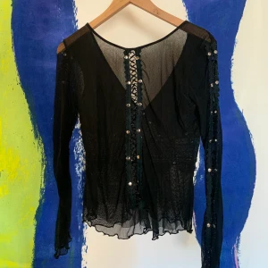SVART TOPP MED SILVERDETALJER - Svart topp med en djup urringning och korsett-liknande detalj där fram med silvriga knappar. På andra bilden syns detaljerna på ärmarna som är densamma som detaljen på ryggen!🙌🏼💗.                                                                       Säljer eftersom att jag inte längre får användning för den, köpt secondhand. Har använt den vid 2 tillfällen. Tröjan är storlek M vilket är en storlek för stort för mig. Superfin topp som går att matcha med det mesta!🌸