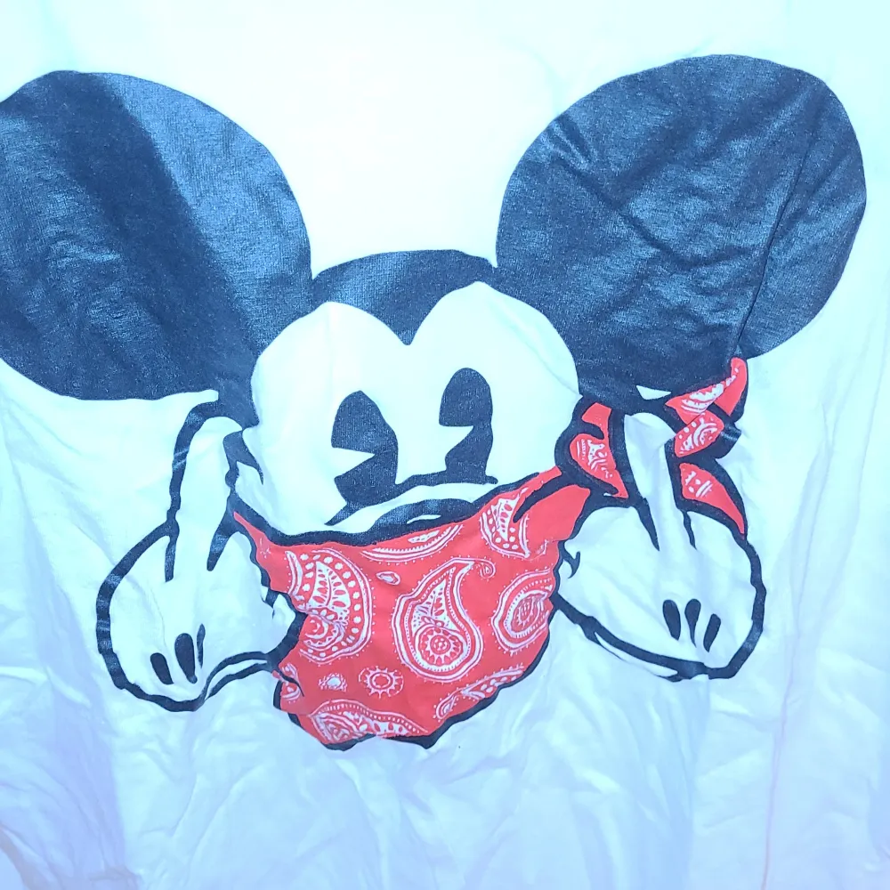 Det är en vit t-shirt men en Mickey Mouse på med röd band runt munnen och sen pekar den med långfigret på båda händerna. . T-shirts.